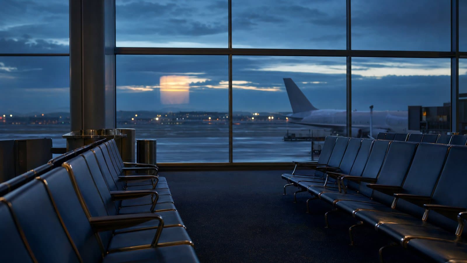 An empty airport departure-gate seating area at dusk with an unmarked plane on the tarmac — in a live Korean investigation, notice of a departure suspension may lawfully be withheld